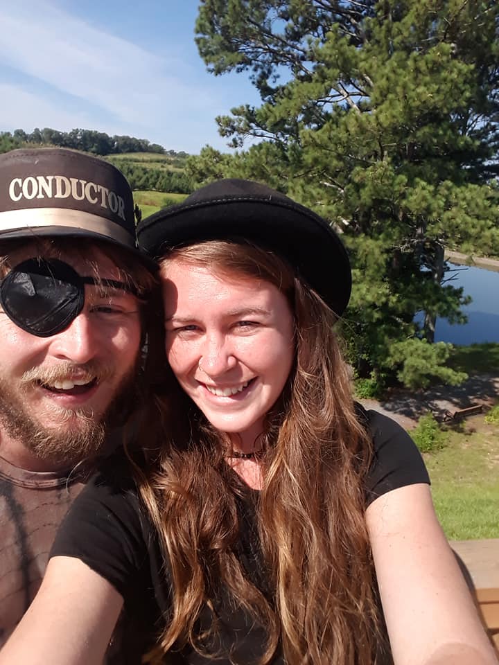 Two friends smiling together in conductor hats on a sunny day